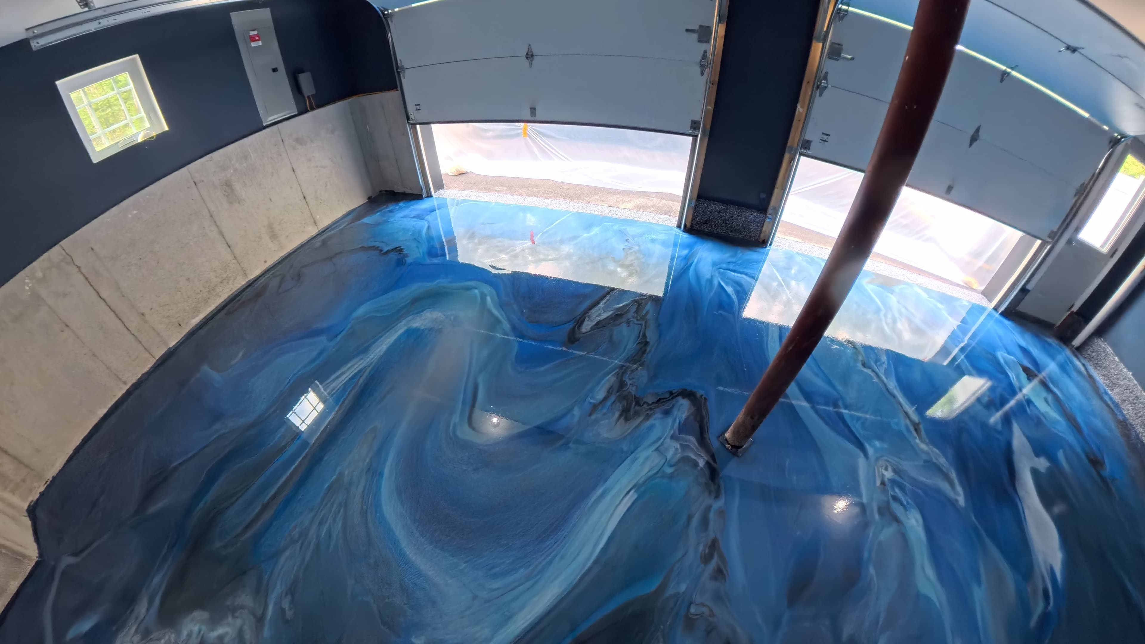 Glossy blue epoxy garage floor reflecting light from the open garage doors in Wallkill, NY